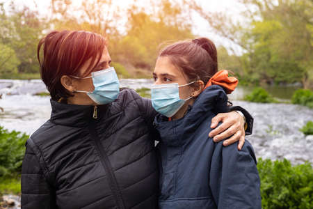 Mother and daughter smiling with the mask in the field next to a creek at dusk with selective focusの写真素材