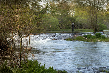 young angler standing at the edge of a small waterfall in a stream fishing and casting in the middle...