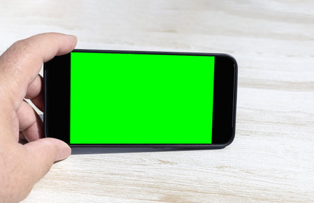 hand holding horizontally a smart phone with a chroma green screen as if watching a video on a light...