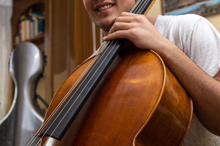 young girl smiling before performing or rehearsing the musical piece with the cello inside the house where the cello case with selective focus can be seen in the background.の写真素材