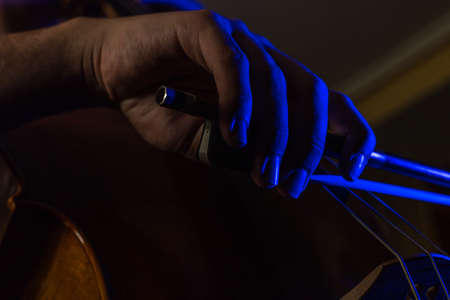 detail of a bowed hand rubbing the strings of a cello with artistic blue lights and selective focusの写真素材