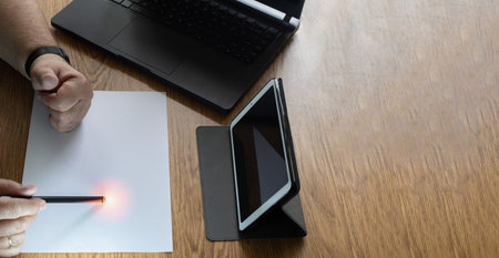 detail of a man working at home with a laptop and tablet to make video calls with a sheet of paper...