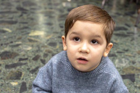 portrait of a small child sitting on the ground and looking astonished as he raises his head with selective focusの写真素材
