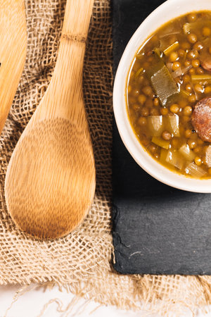 detail of a photo from above of a deep dish of lentils, leeks and chorizo along with a wooden spoon ready to eat.の写真素材
