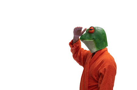 young boy wearing a green frog animal mask with orange bathrobe with hand on face watching or looking like a pirate lookout on white background with copy space concept watchingの写真素材