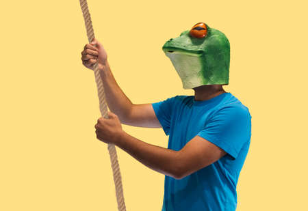 person gesture with frog mask holding with both hands a rope rope for holding or catching objects on yellow background with copy spaceの写真素材