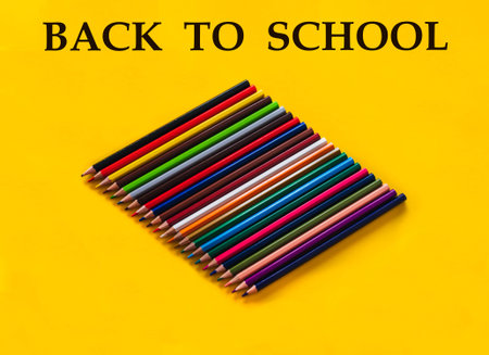 composition of wooden pencils in different colors and shades on a yellow background and the letters...