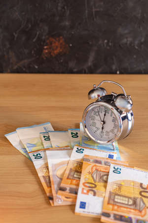 analog clock on a table with money of different amounts of euros concept time of economy and savingsの写真素材