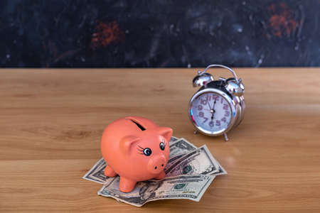 money in dollar bills placed under a piggy bank and a clock with a selective focus concept time saving conceptの写真素材