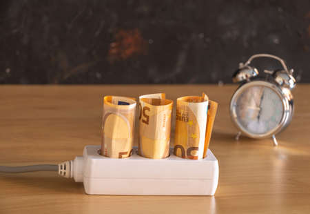 50 euro banknotes rolled up in the sockets and a clock in the background showing the time with selective light bulb concept economia electricityの写真素材