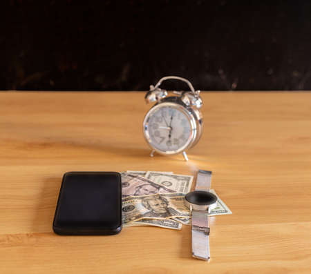 mobile phone and smart watch placed on dollar money on a table with a selective focus analog clockの写真素材