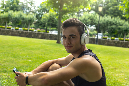 portrait of an athletic Caucasian boy sitting listening to mobile phone music through white...