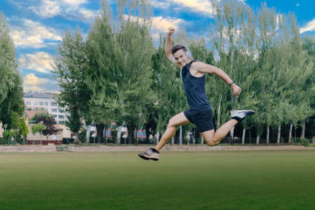 cheerful young athlete jumping while listening to music through white headphones in the middle of a garden with copy space.の写真素材