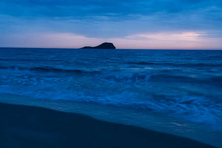 sunrise on a beach with an island at the bottom of the horizon with silky water and bluish huesの写真素材