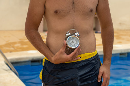 young caucasian man in swimsuit with a watch at stomach level near the pool concept digestion time