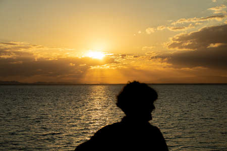 Black silhouette of a woman in a sunset on the beach with the sea and the sun.の写真素材