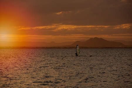 black silhouette of a man windsurfing with sail at sunset at seaの写真素材