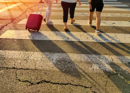 family crossing the road at the crosswalk with a red suitcase on a sunny day at sunset