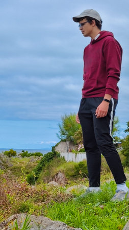 young adult with cap looking over the cliff with the sea in the background