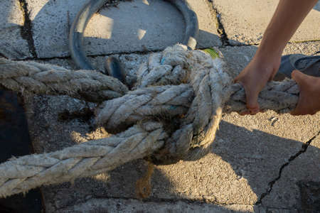 detail of a person pulling a rope or rope with sailors knots to moor the ship in the harbor on a metal bollardの写真素材