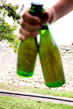 hand picking up two green bottles of beer or cider concept to share with friendsの写真素材