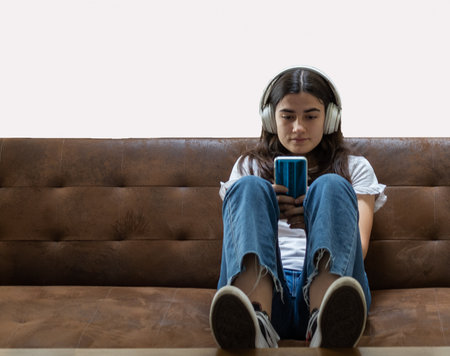 girl sitting on the sofa using mobile phone with headphonesの写真素材