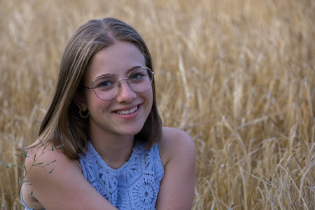 smiling, attractive young girl with glasses sitting in wheat fieldの写真素材