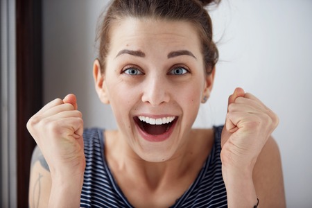 Surprised woman with hands up amazed or shocked by unexpected news holding close palms up and showing happy expression. Young adult woman on greybackground Surprised woman with hands up amazed or shocked by unexpected news holding close palms up and showing happy expression. Young adult woman on greybackground