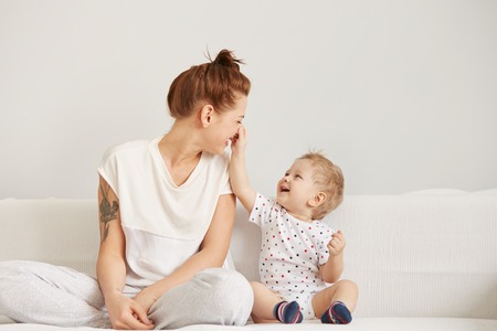 Young mother with her one years old little son dressed in pajamas are relaxing and playing in the bedroom at the weekend together, lazy morning, warm and cozy scene. Selective focus.