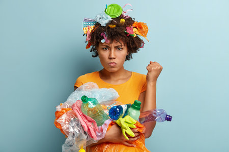 Image of annoyed black woman raises clenched fist, demands to be environmentally friendly, has...