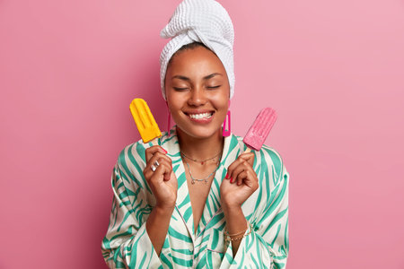 Pleased dark skinned woman bites lips, holds tasty appetizing ice cream, imagines pleasant taste of...