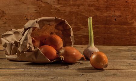 Against the background of old boards is garlic and onion in a kraft bagの写真素材