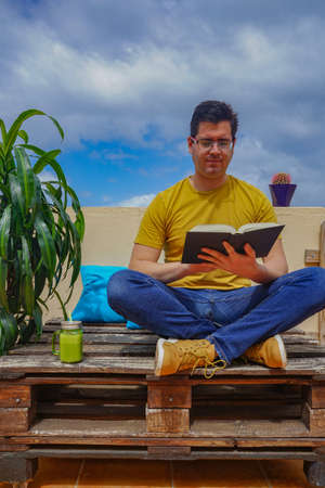 Man reading a book on the balcony of his house. He is drinking a strawberry juice.の写真素材