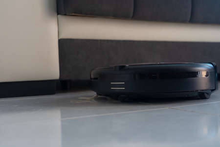 Robot vacuum cleaner automatically cleaning the floor. In the background, there is a couch.の写真素材