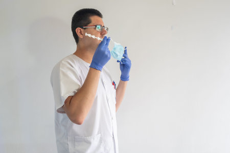 Doctor / nurse putting on a mask to protect against the coronavirus. He is wearing blue gloves and...