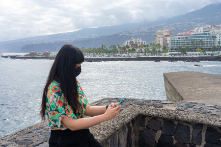 Asian tourist chatting with her smartphone. She does tourism in Puerto De La Cruz, Tenerife. She...