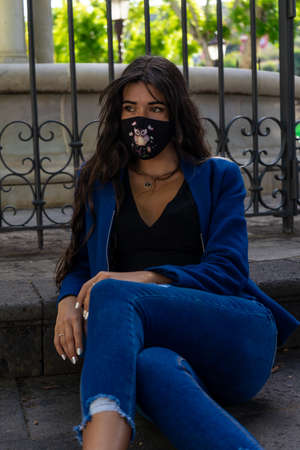 Young woman posing for a portrait sitting on the floor. She wears heels, jeans and an American jacket. In the background you can see a fountain from La Laguna, Tenerife.の写真素材