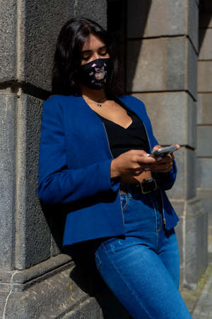 Young woman chatting with her smartphone. She wears jeans and an blue American jacket. The photo was taken in La Laguna, Tenerife.の写真素材