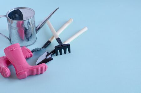 Creative garden tools - a metal watering can, a rake, shovels, rubber boots are on a blue background. horizontal image, minimalismの写真素材