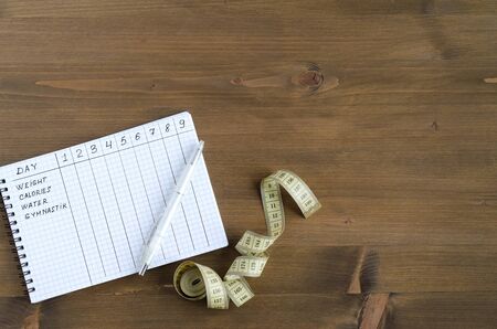 The diary we lose weight at home and a measuring tape lie on a wooden table. Copy space. Healthy lifestyle concept.の写真素材