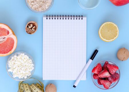 Diary copy space lies on a blue background. Strawberries, lemon, cottage cheese, grapefruit, walnuts lie nearby. Healthy lifestyle concept.の写真素材