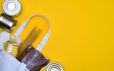 Products in packages sugar, buckwheat, pasta, oil in a bottle in an eco bag are on a yellow background. The concept of delivery of the necessary products during quarantine, self-isolation. Copyspace.の写真素材