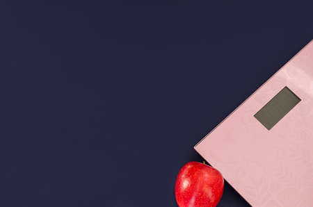 Weight control concept. Scales and apple on dark blue background, trend blue color 2020, flat lay, copy spaceの写真素材