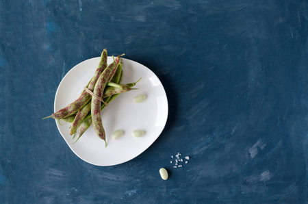 Green bean pods tied with jute lie on a white plate and on a blue background. Copy space, space for...