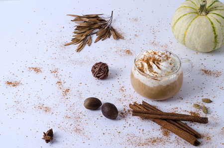 Pumpkin latte in a small glass mug with cream and cinnamon. Cozy warm autumn drink concept with...