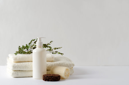 A stack of cream-colored COTTON TOWELS on a white background with cosmetic accessories. Concept for...