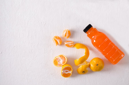 Fresh tangerines fruits and tangerine juice in a bottle on a structural light background. Food background with flat lay and copy spaceの写真素材