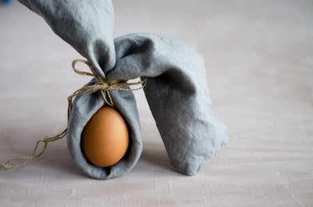 Creative Easter bunny, natural unpainted chicken egg is wrapped in a gray napkin and stands on a...