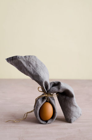 Creative Easter bunny, natural unpainted chicken egg is wrapped in a gray napkin and stands on a...