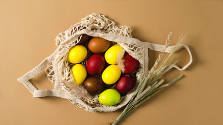 Colorful Easter chicken eggs lie in an eco-bag on a beige background with a bouquet of dried herbs,...